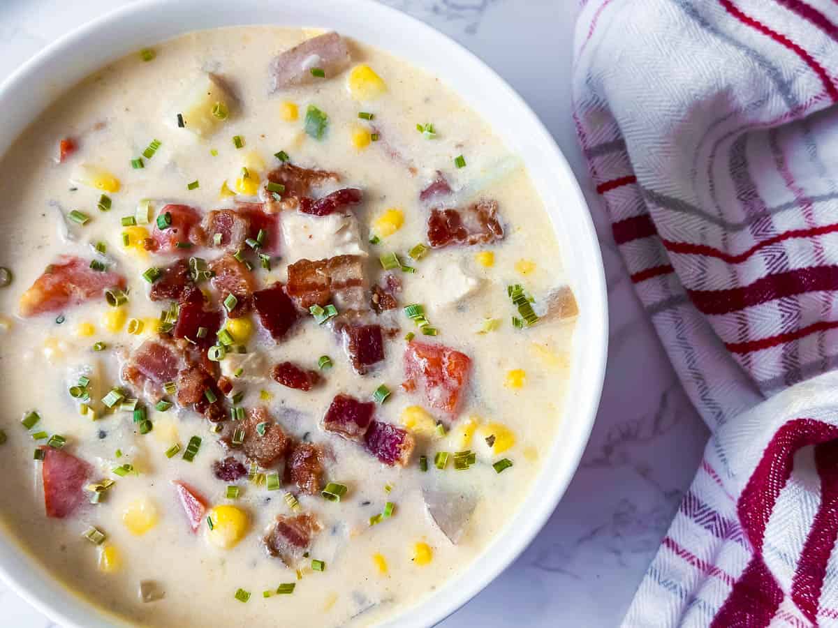 Chicken corn chowder in a bowl with chopped bacon and chives on top.