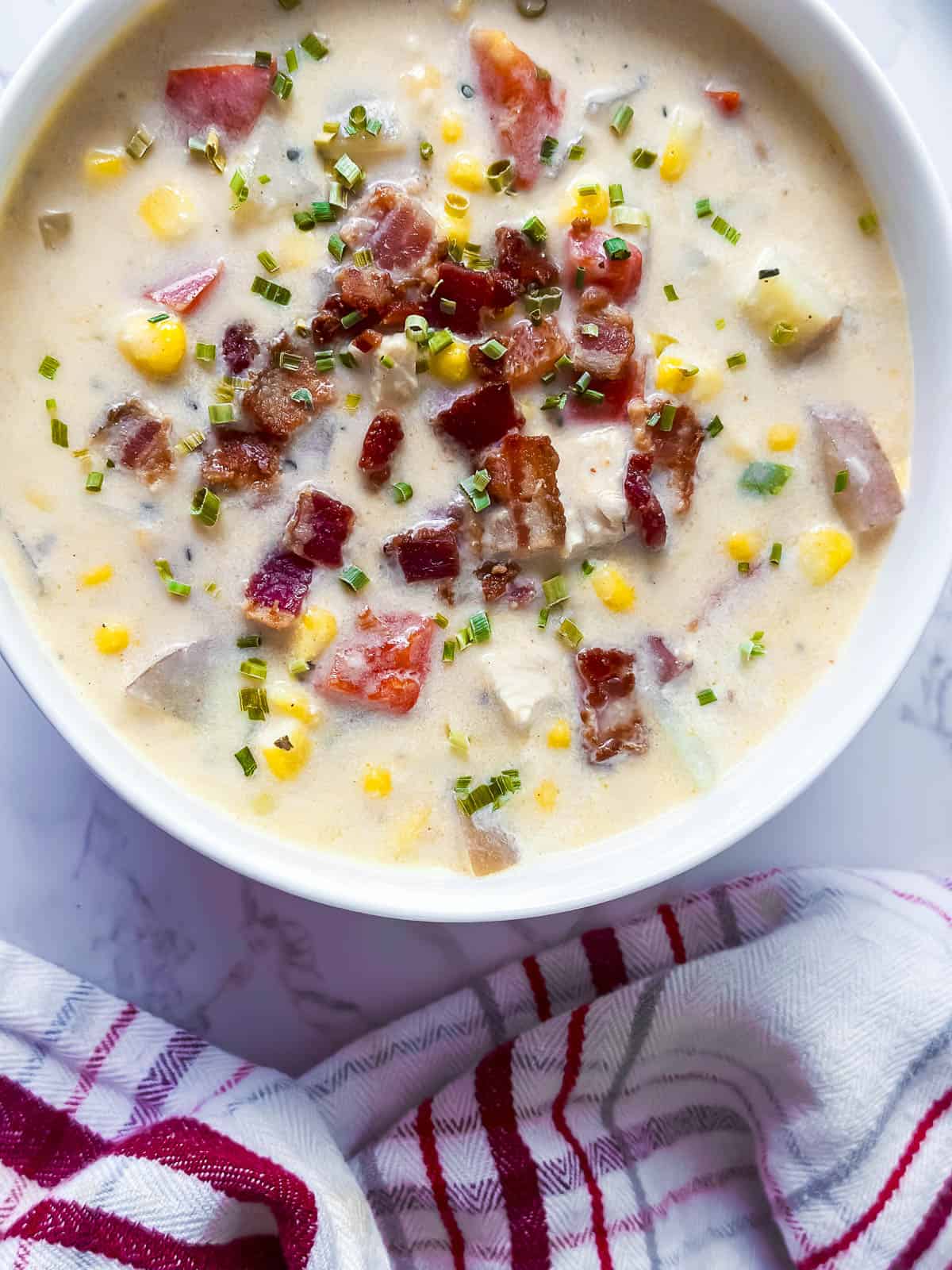Creamy chicken corn chowder in a white bowl with a red and white napkin.
