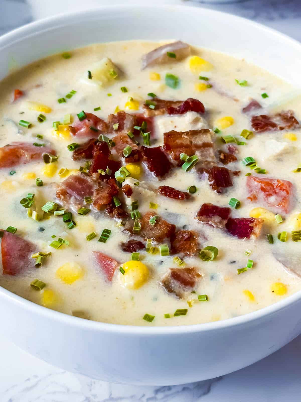 Three-quarter view of chicken corn chowder in a white bowl with bacon and chives on top.