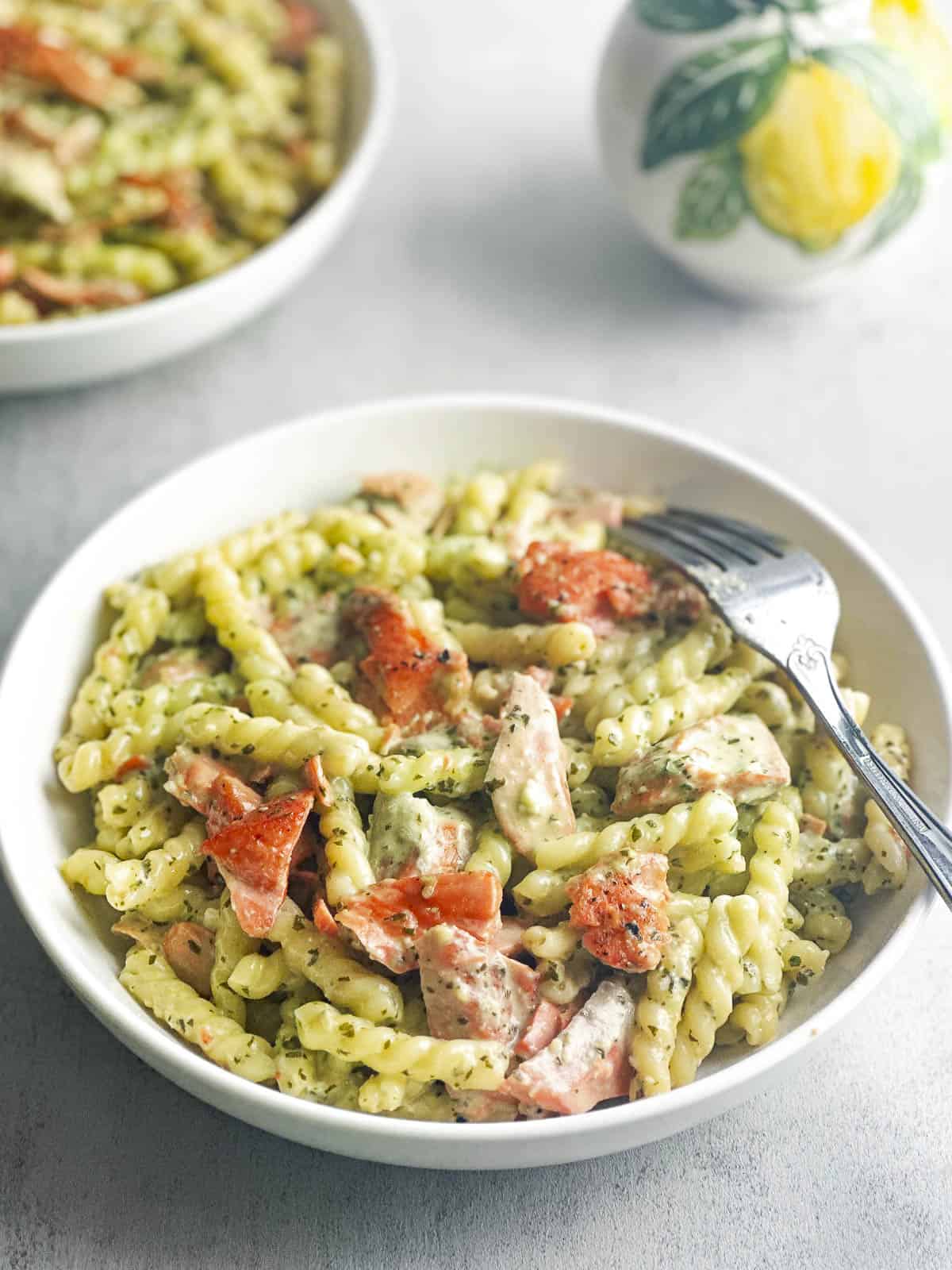 Pesto salmon pasta in a white bowl with a fork.