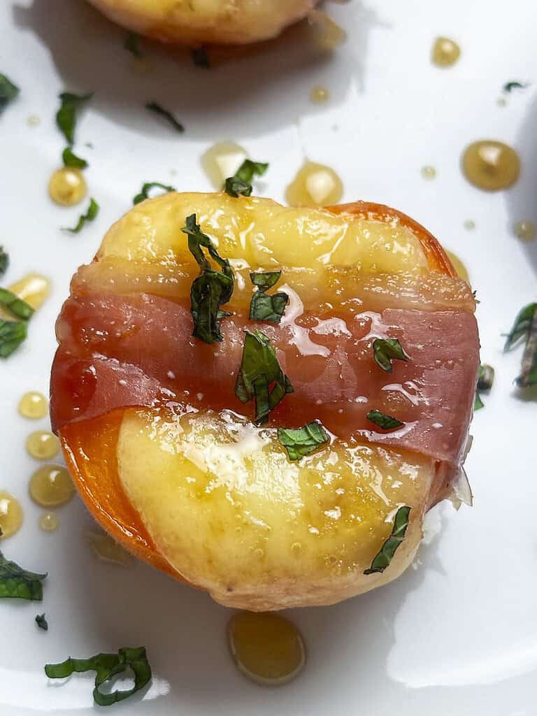 A prosciutto wrapped apricot with cheese, honey, and fresh mint leaves.
