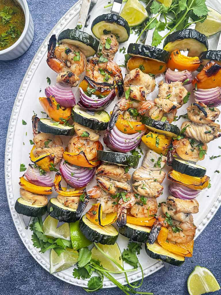 Grilled shrimp and chicken skewers with veggies and marinade on the side.