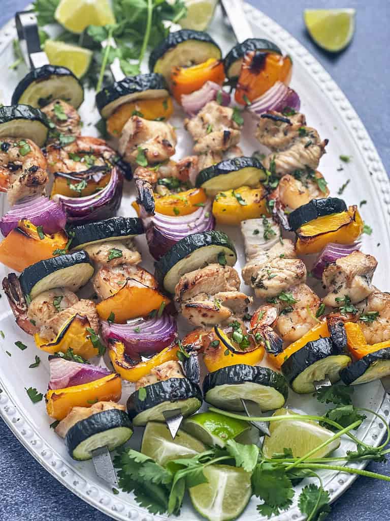 Grilled shrimp and chicken skewers with veggies on a white plate.