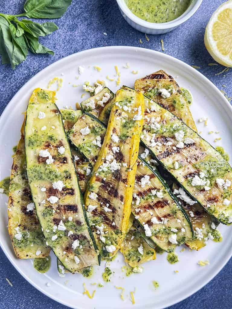Grilled summer squash and zucchini on a plate with lemon basil sauce and crumbled feta.
