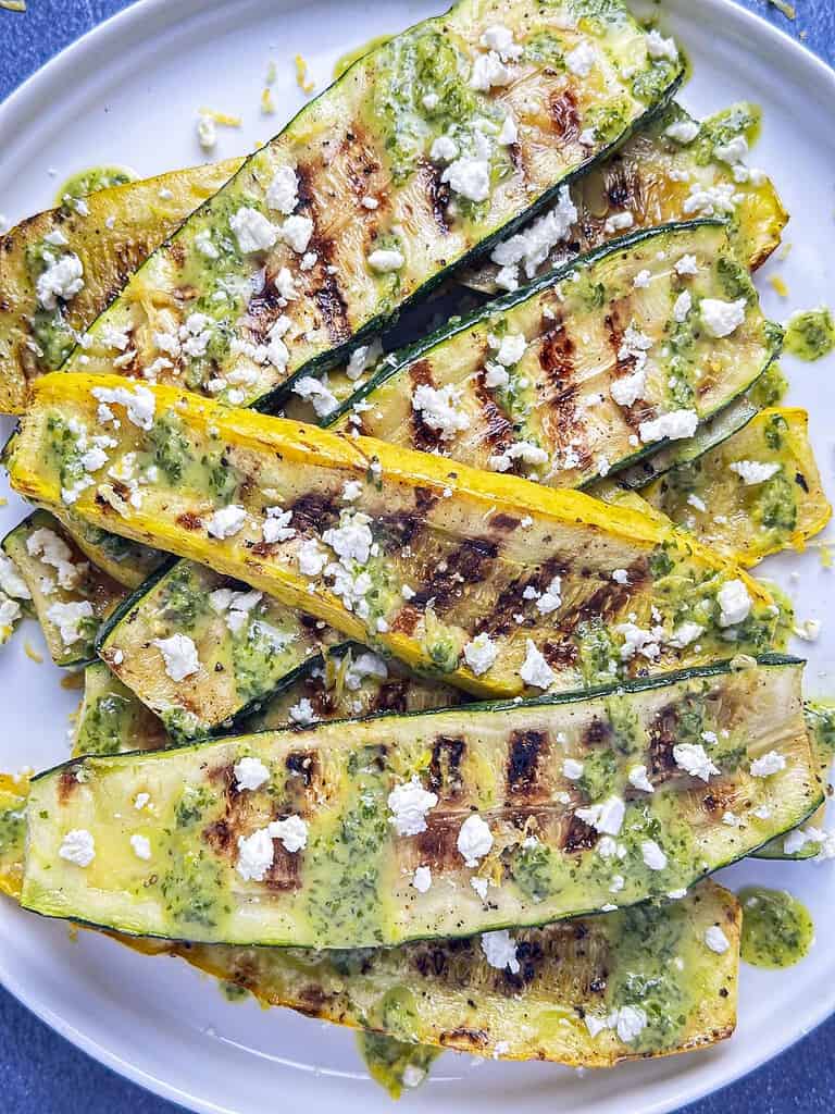 Grilled summer squash and zucchini on a plate with lemon basil drizzle and crumbled feta.