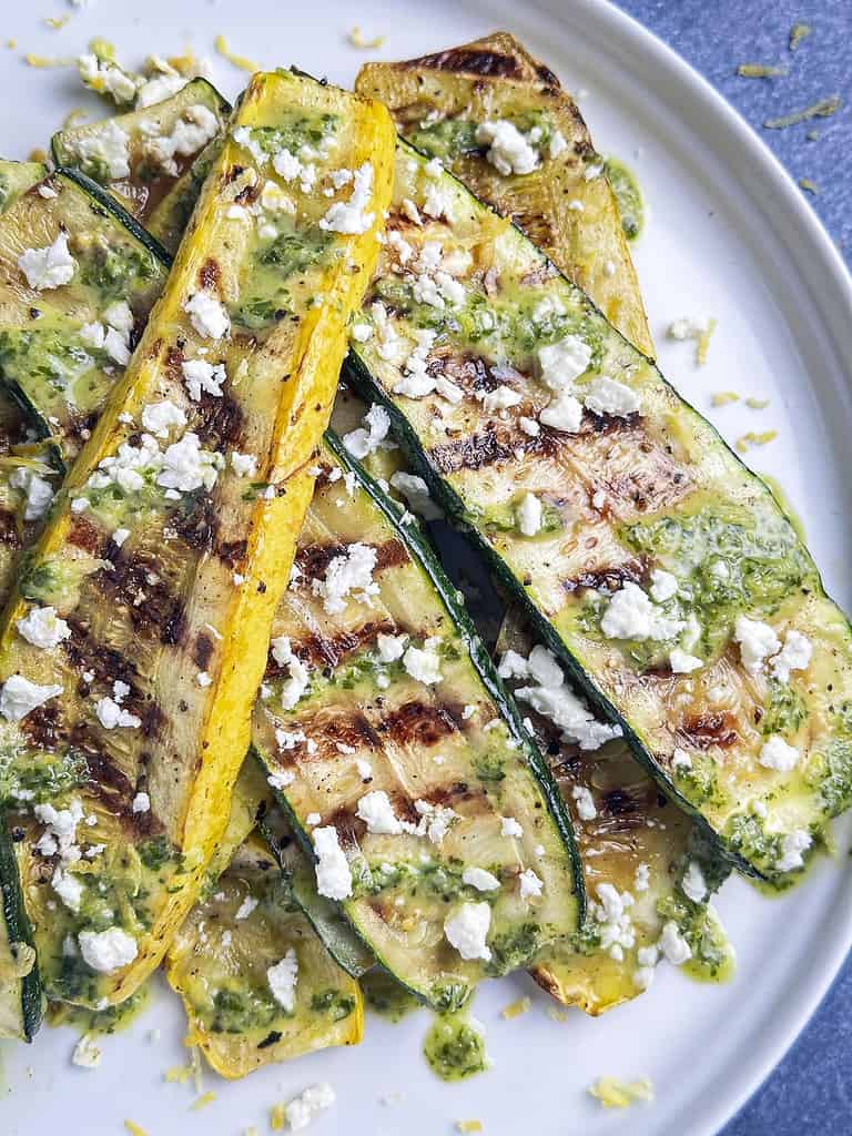 Grilled summer squash and zucchini on a plate with lemon basil sauce and crumbled feta.