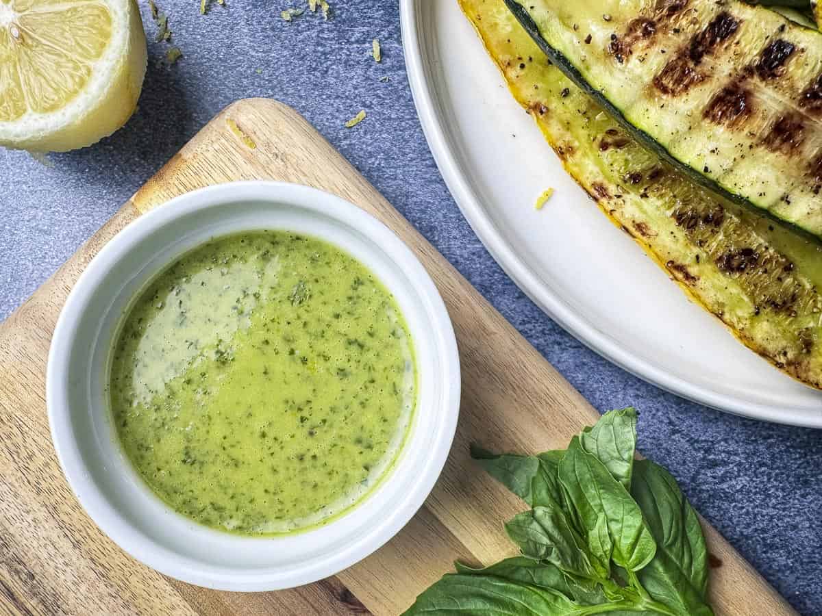 Lemon basil sauce in a ramekin with basil and lemon on the side.