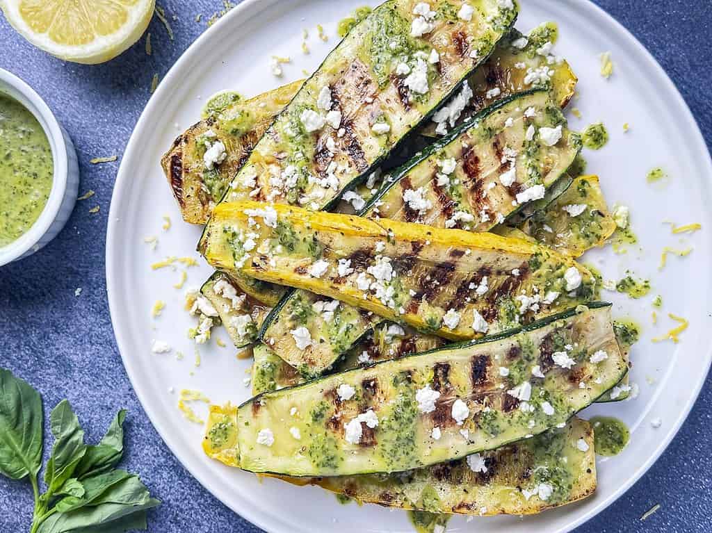 Grilled summer squash and zucchini on a plate with lemon basil sauce and crumbled feta.