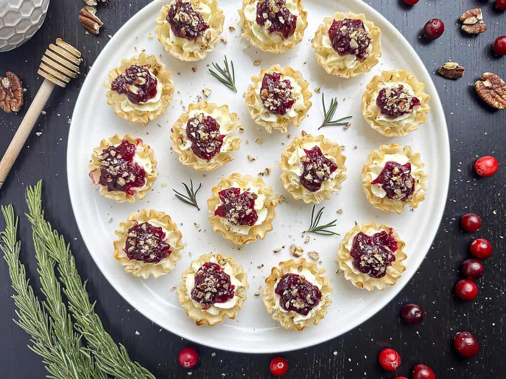 Cranberry tartlets on a round white plate with rosemary and cranberries surrounding.