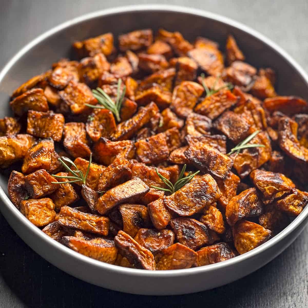 Roasted sweet potatoes with fresh rosemary in a grey bowl