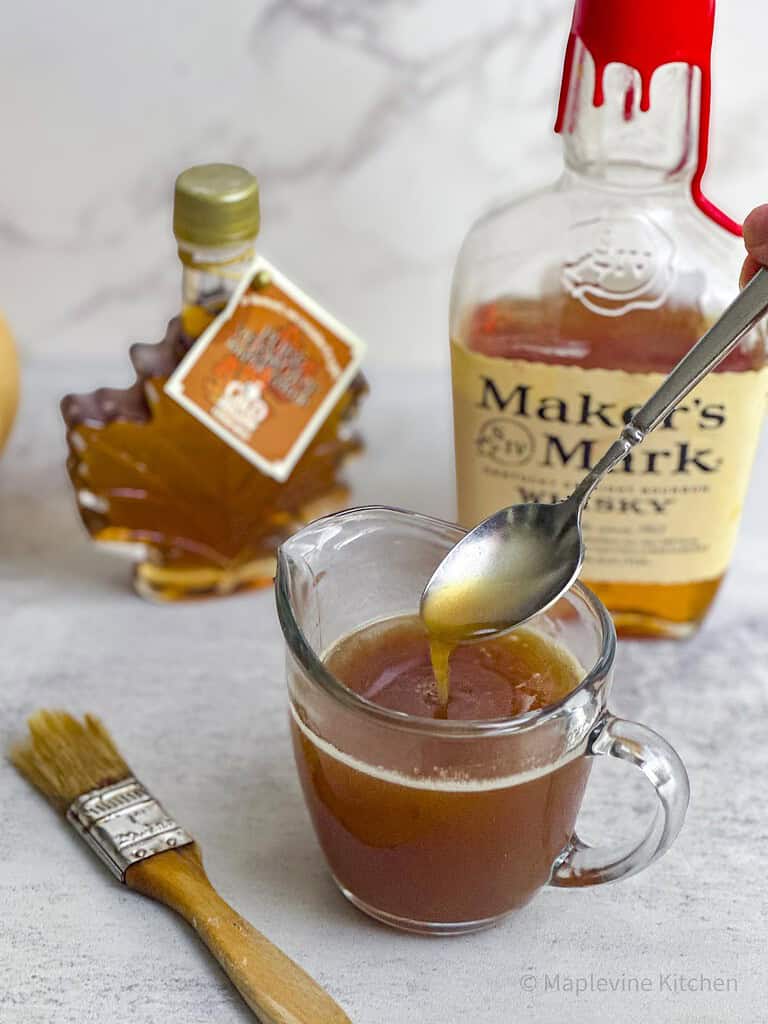 Maple bourbon glaze in a carafe with a spoon.