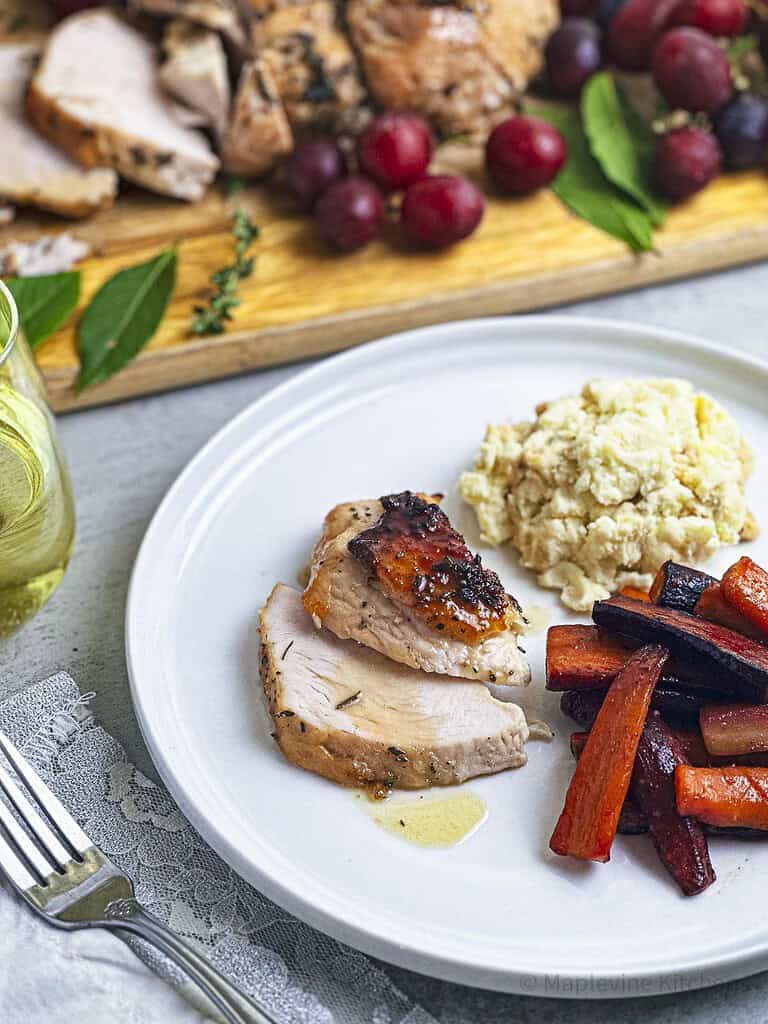 Maple bourbon glazed turkey breast on a white plate with mashed potatoes and roasted carrots.