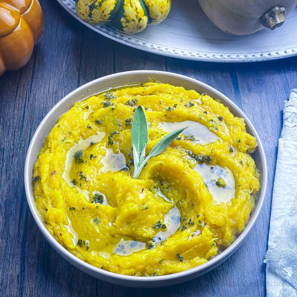 Mashed acorn squash in a grea bowl with brown butter and sage on top