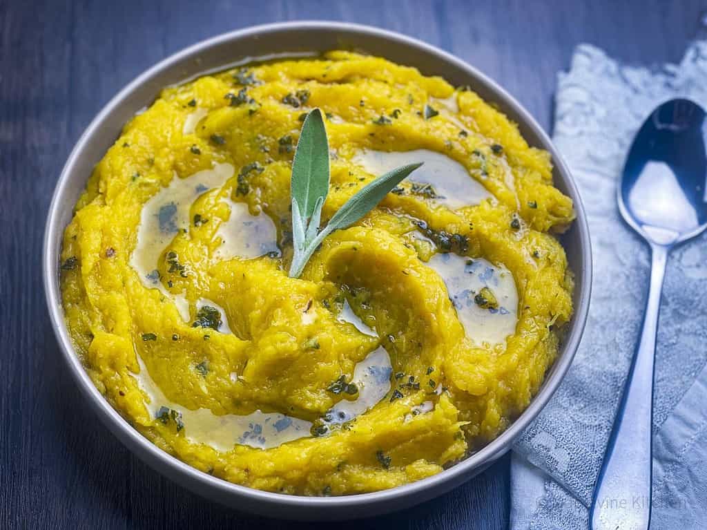 Mashed acorn squash with sage in a bowl and a spoon on the side.