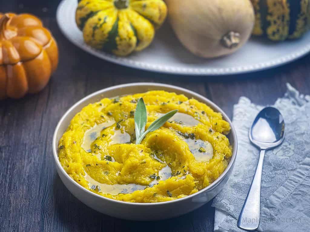 Mashed acorn squash with brown butter and sage in a bowl with a spoon on the side.