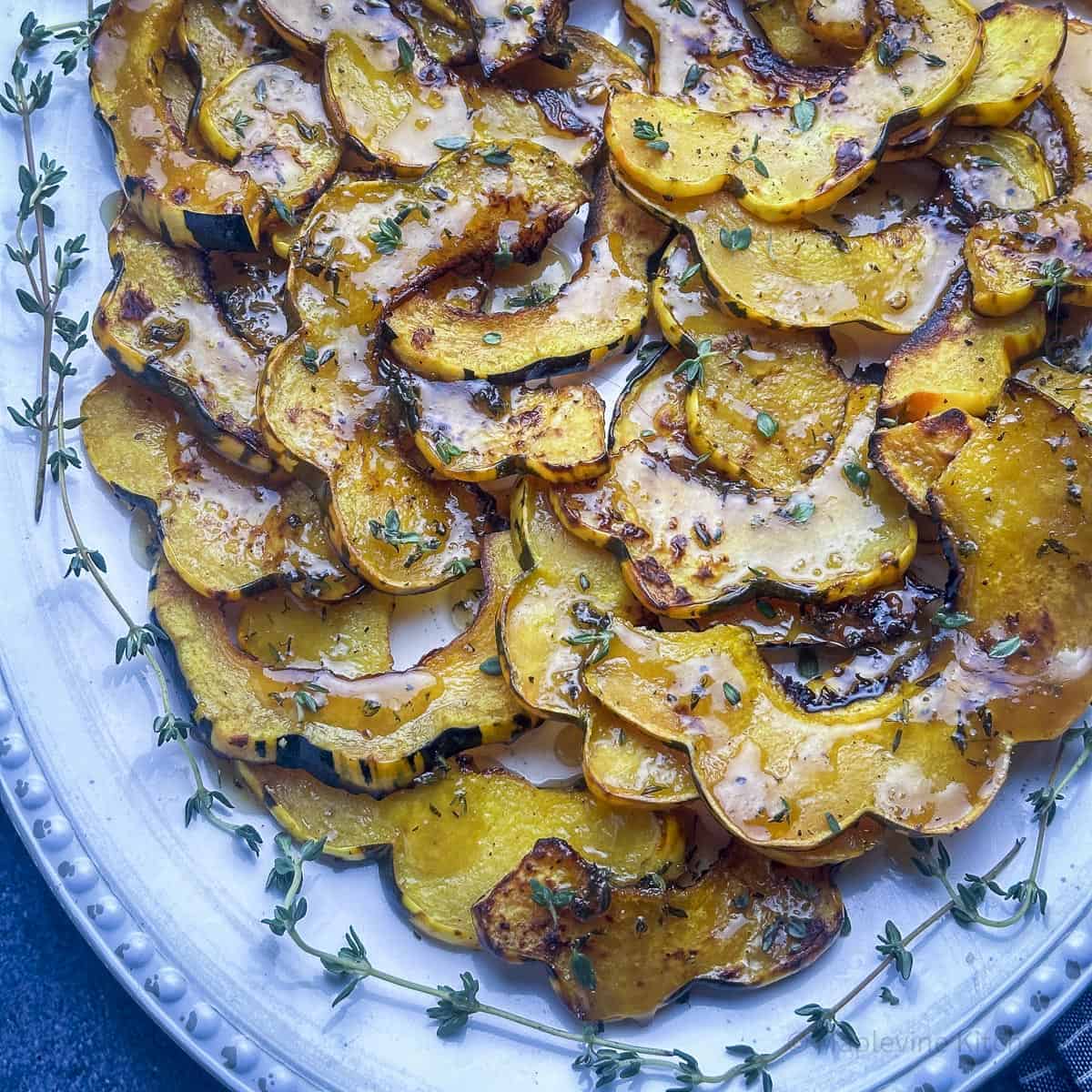 Maple glazed roasted delicata squash slices layered on a white platter with fresh thyme