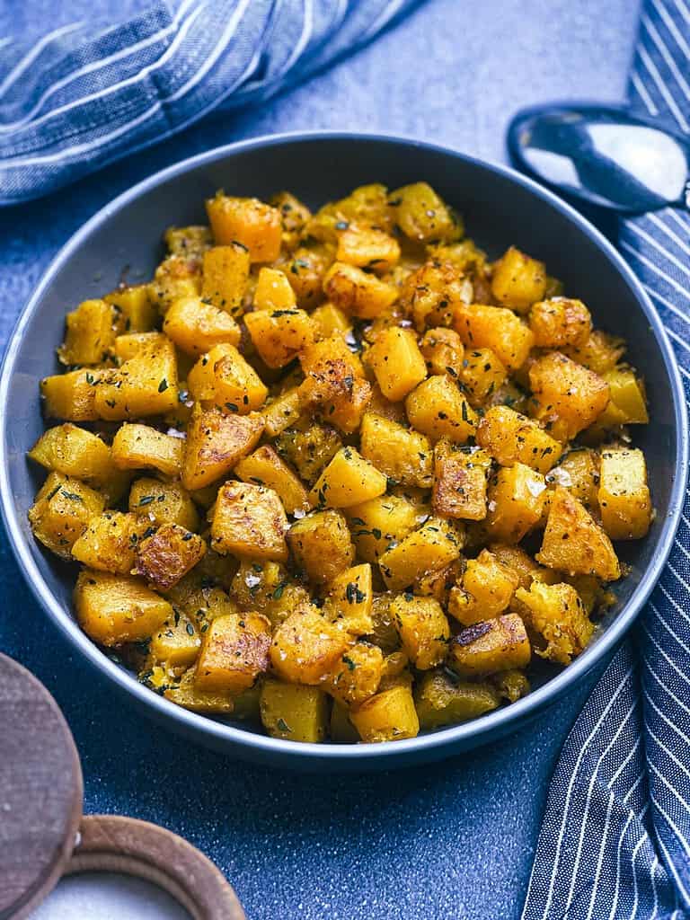Sauteed butternut squash in a bowl with napkins and spoon.