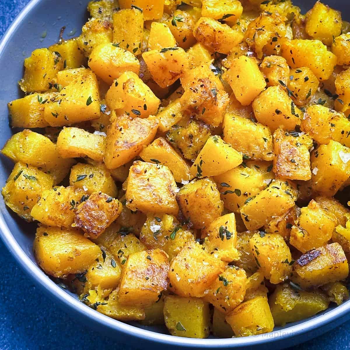 Roasted butternut squash cubes with flaky salt and herbs in a grey bowl