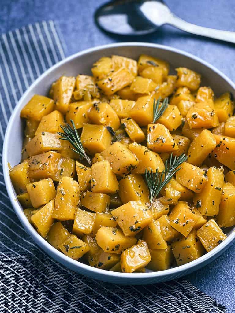 Butternut squash with apple cider glaze in a bowl with a spoon above.