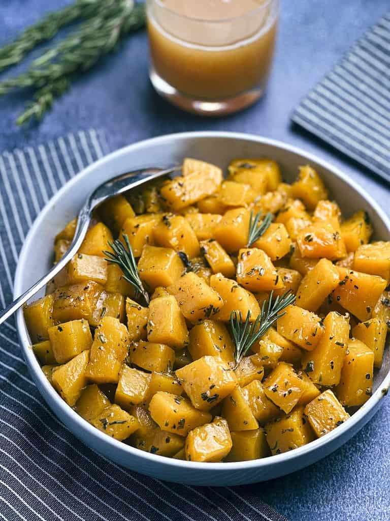 Butternut squash with apple cider glaze in a bowl with a glass of cider on the side.