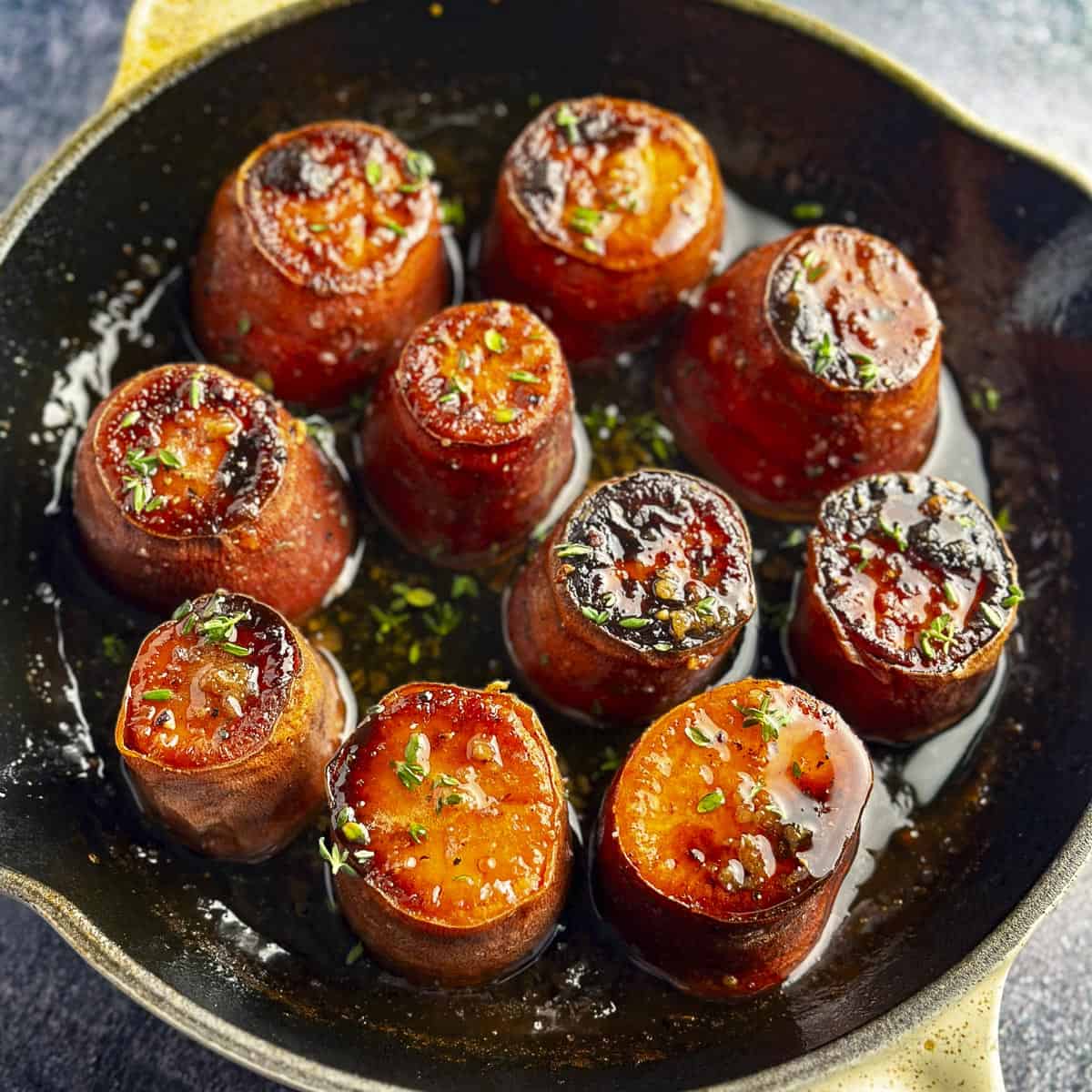 Maple glazed sweet potato rounds in a cast iron skillet with fresh herb garnish