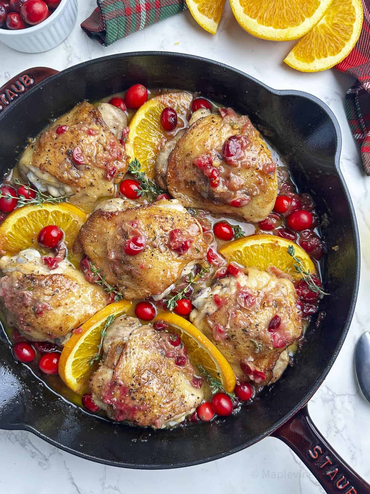 Chicken thighs with cranberries and orange slices in a cast iron skillet.