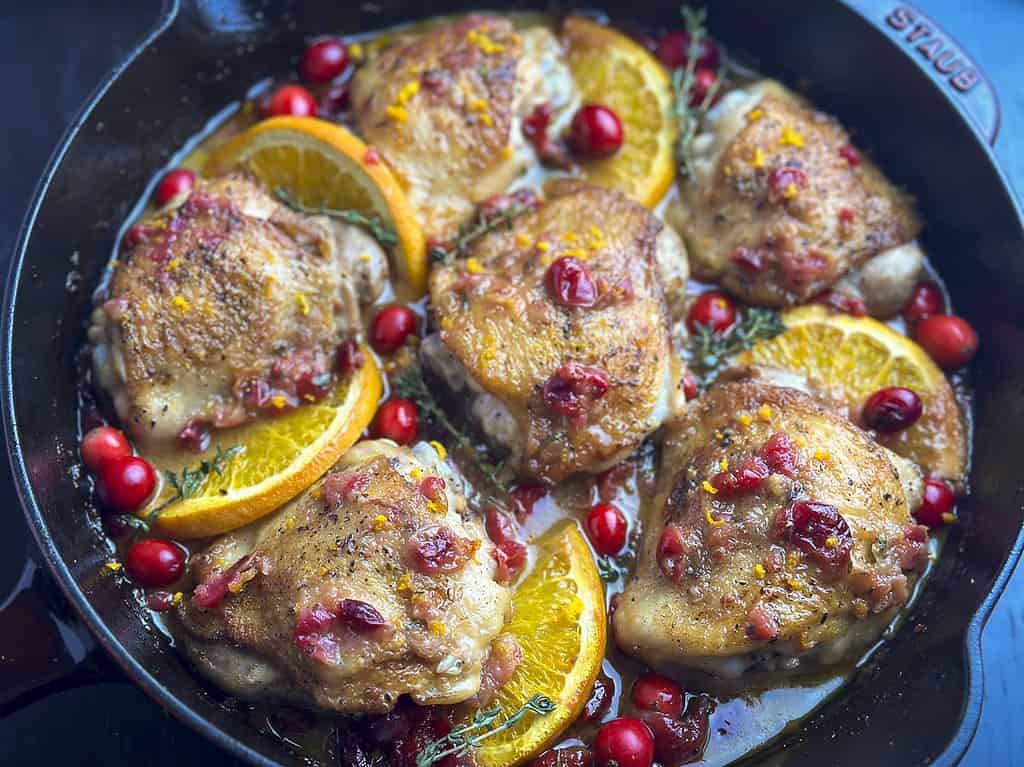 Bone-in chicken thighs with cranberries and orange in a cast iron skillet.