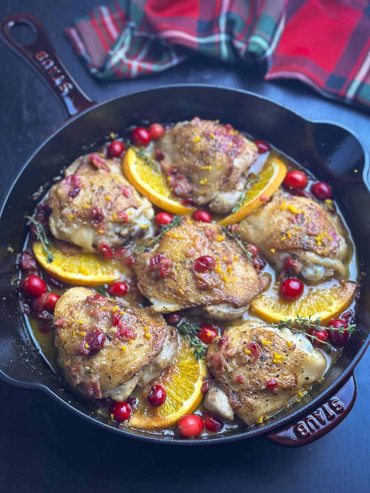 Seared chicken thighs in a cast iron skillet with cranberries and oranges.