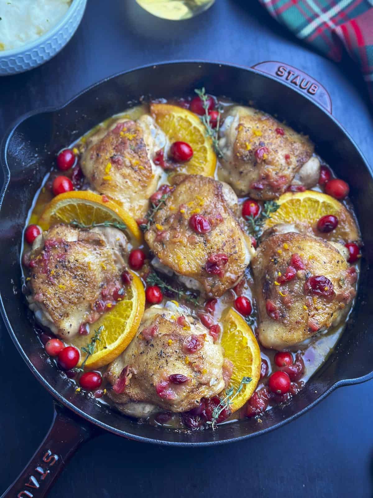 Chicken thighs in a Staub skillet with cranberries, oranges, and fresh thyme.