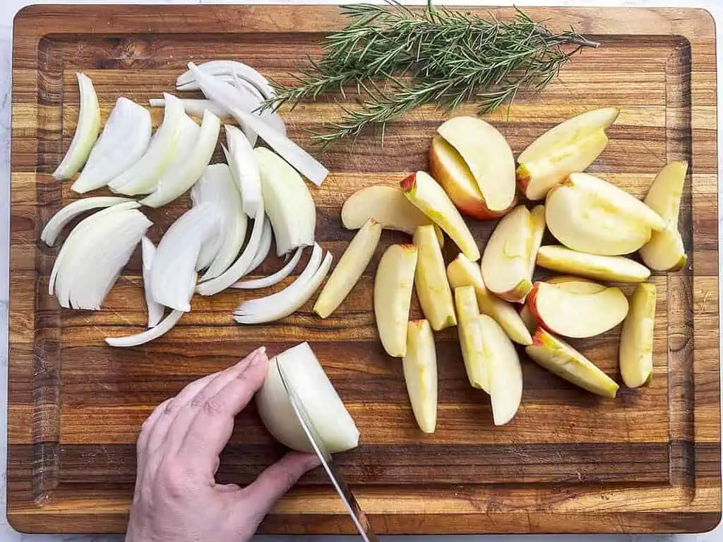 Cutting board with hand slicing onion and slices of onion and apples.