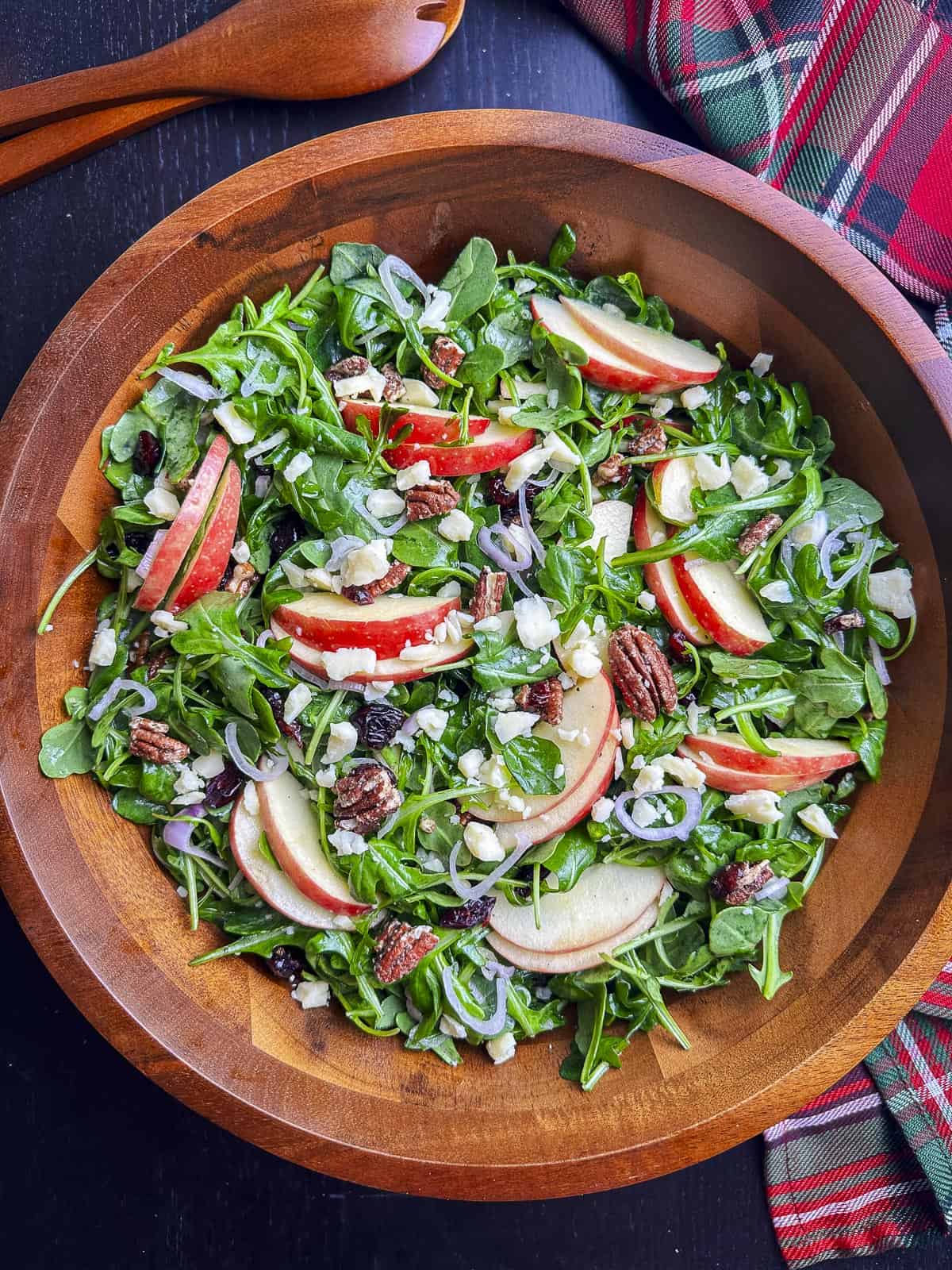 Arugula salad with apples, cheddar, pecans, and cranberries in a wooden bowl.