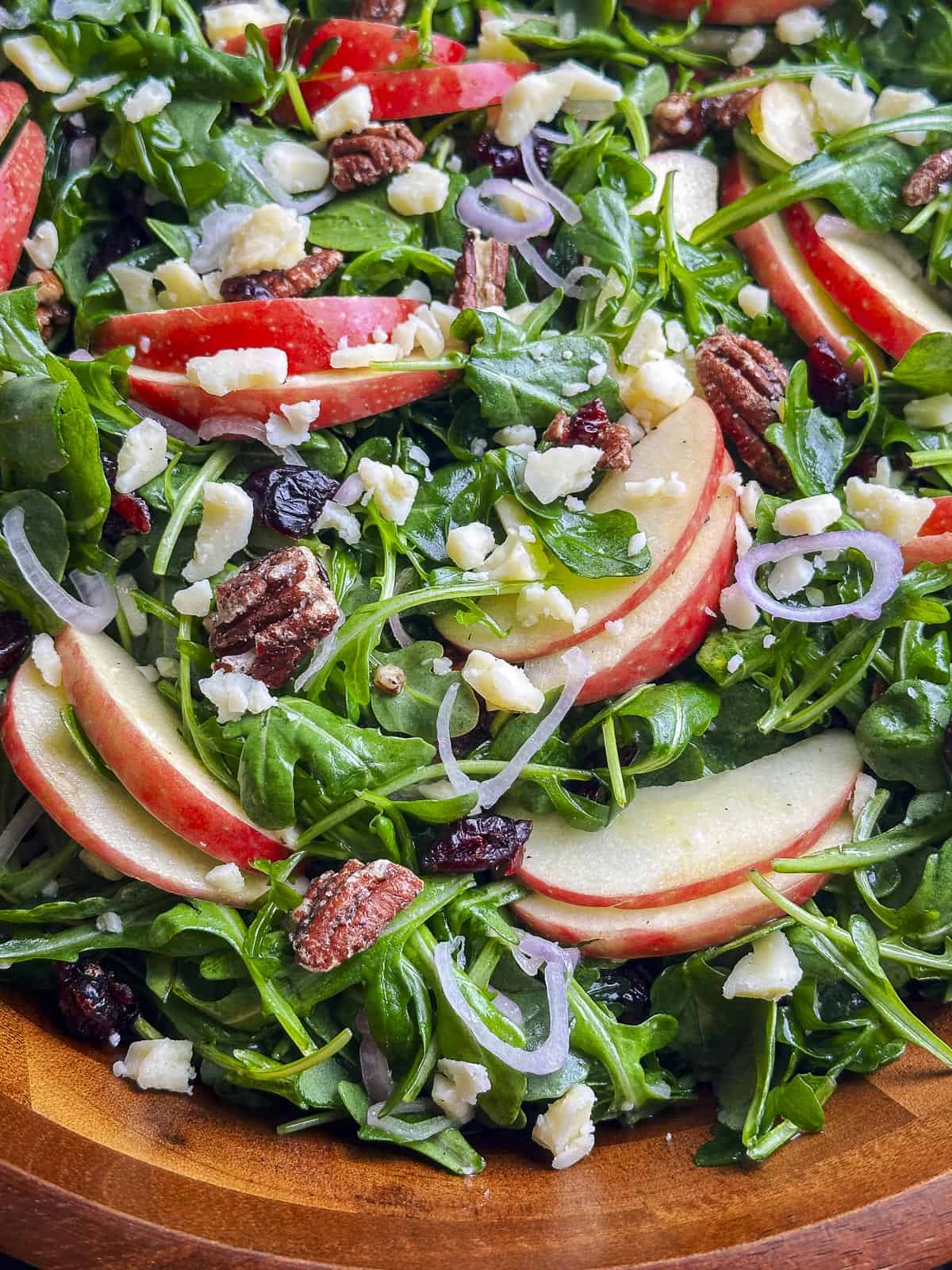 Arugula salad with apples, cheddar, pecans, and cranberries in a wooden bowl.
