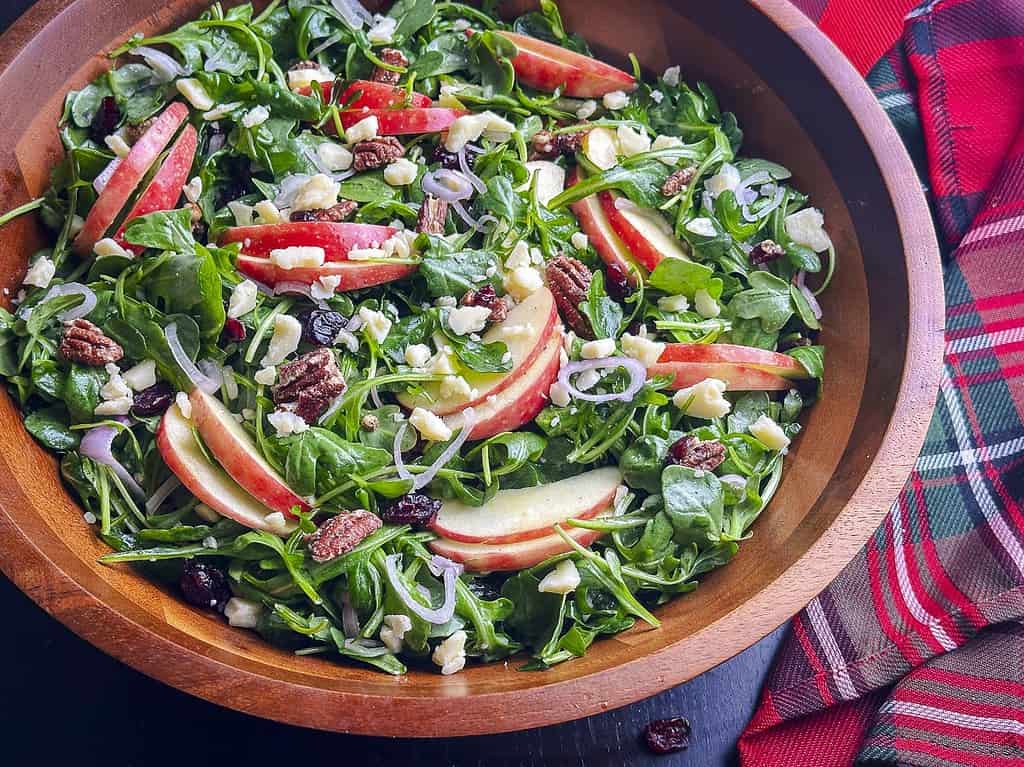 Arugula salad with apples, cheddar, pecans, and cranberries in a wooden bowl.