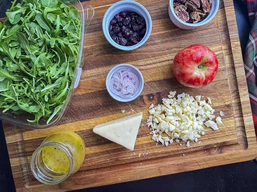Ingredients for arugula apple salad on a wooden cutting board.