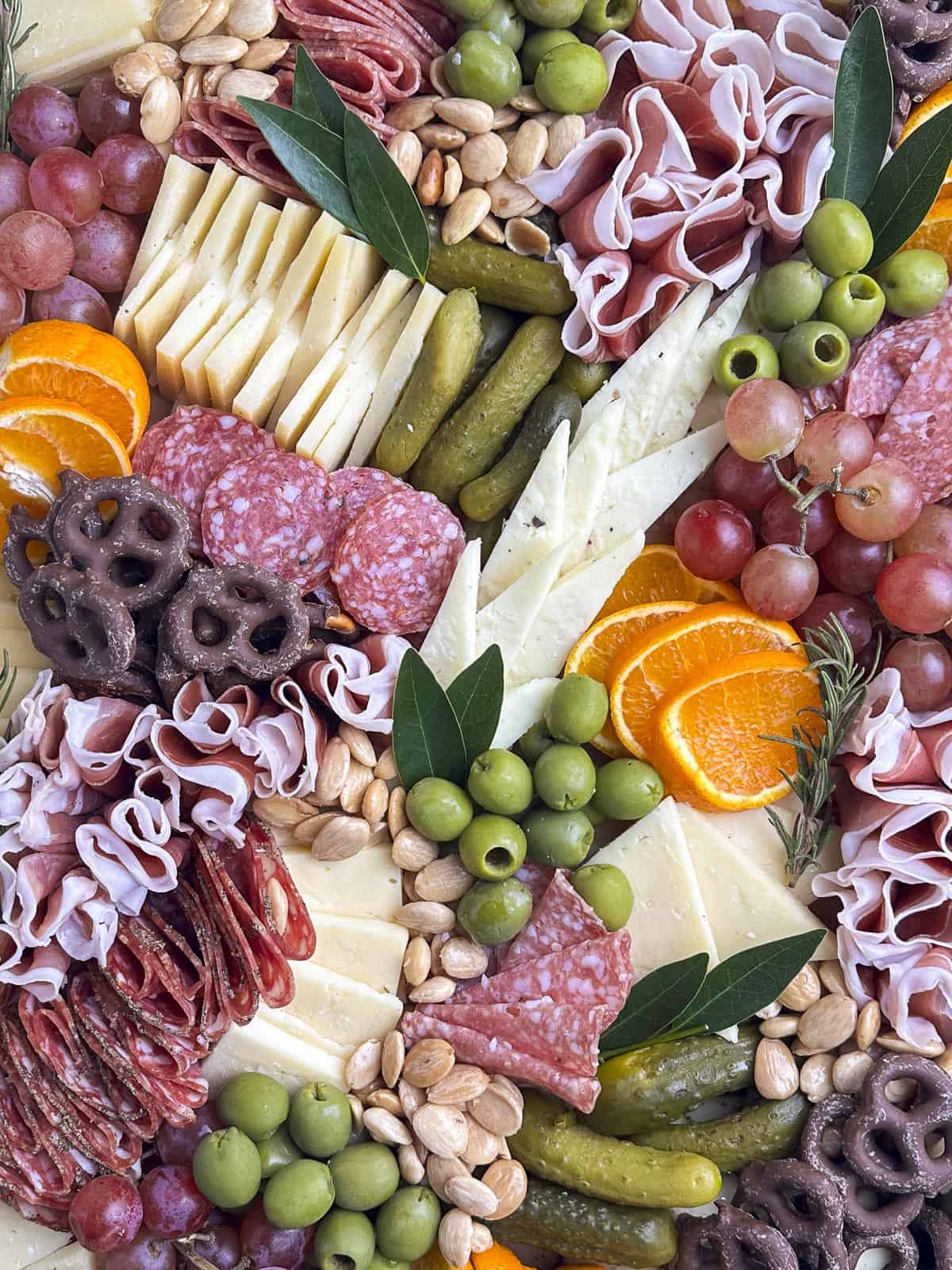 Salami, prosciutto, cheese, fruit, olives, pickles, and nuts arranged on a wooden charcuterie board,