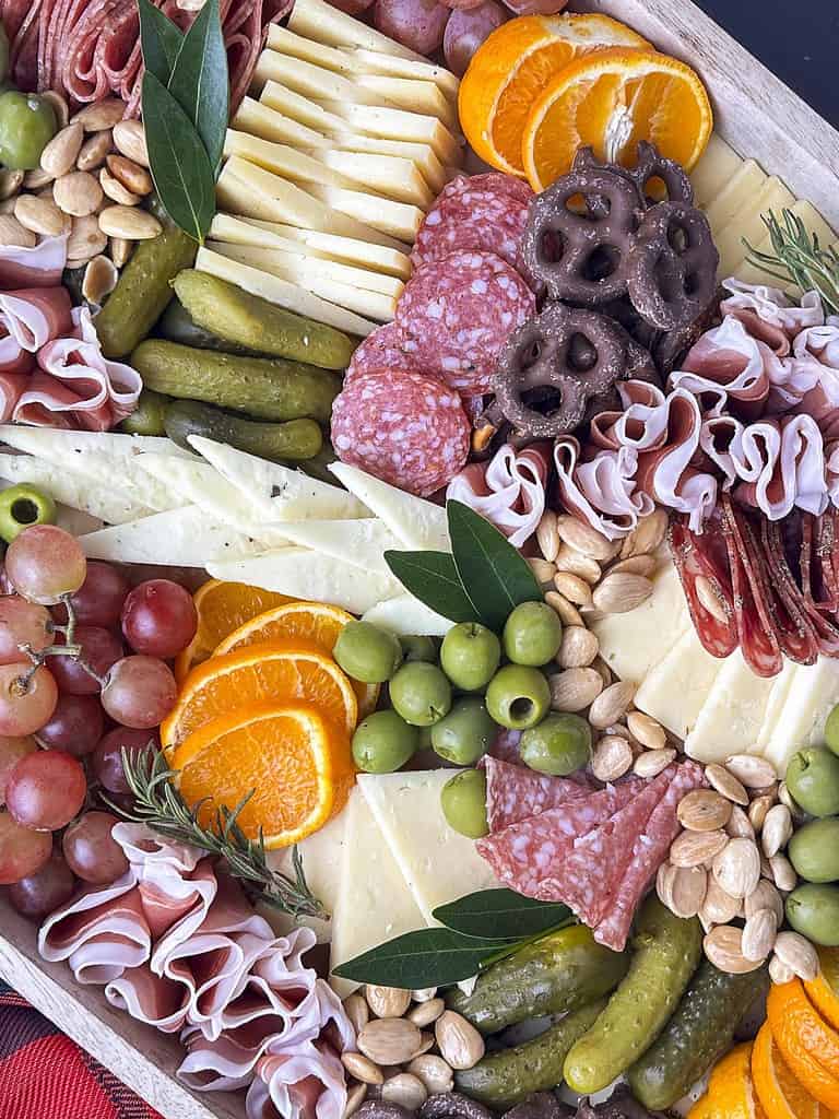 Charcuterie meats, cheese, fruit, olives, pickles, and nuts on a wooden tray,