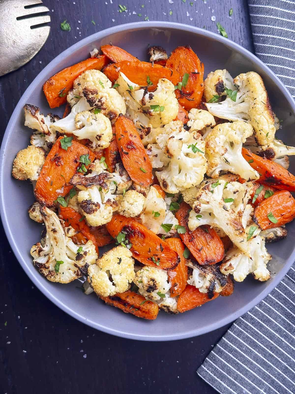 Overhead shot of roasted carrots and cauliflower in a bowl with a little parsley on top.