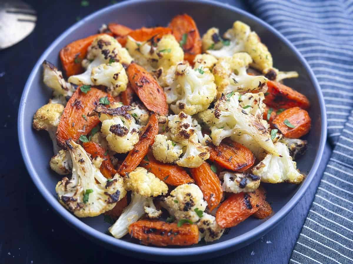 Roasted carrots and cauliflower in a bowl with a napkin on the side.