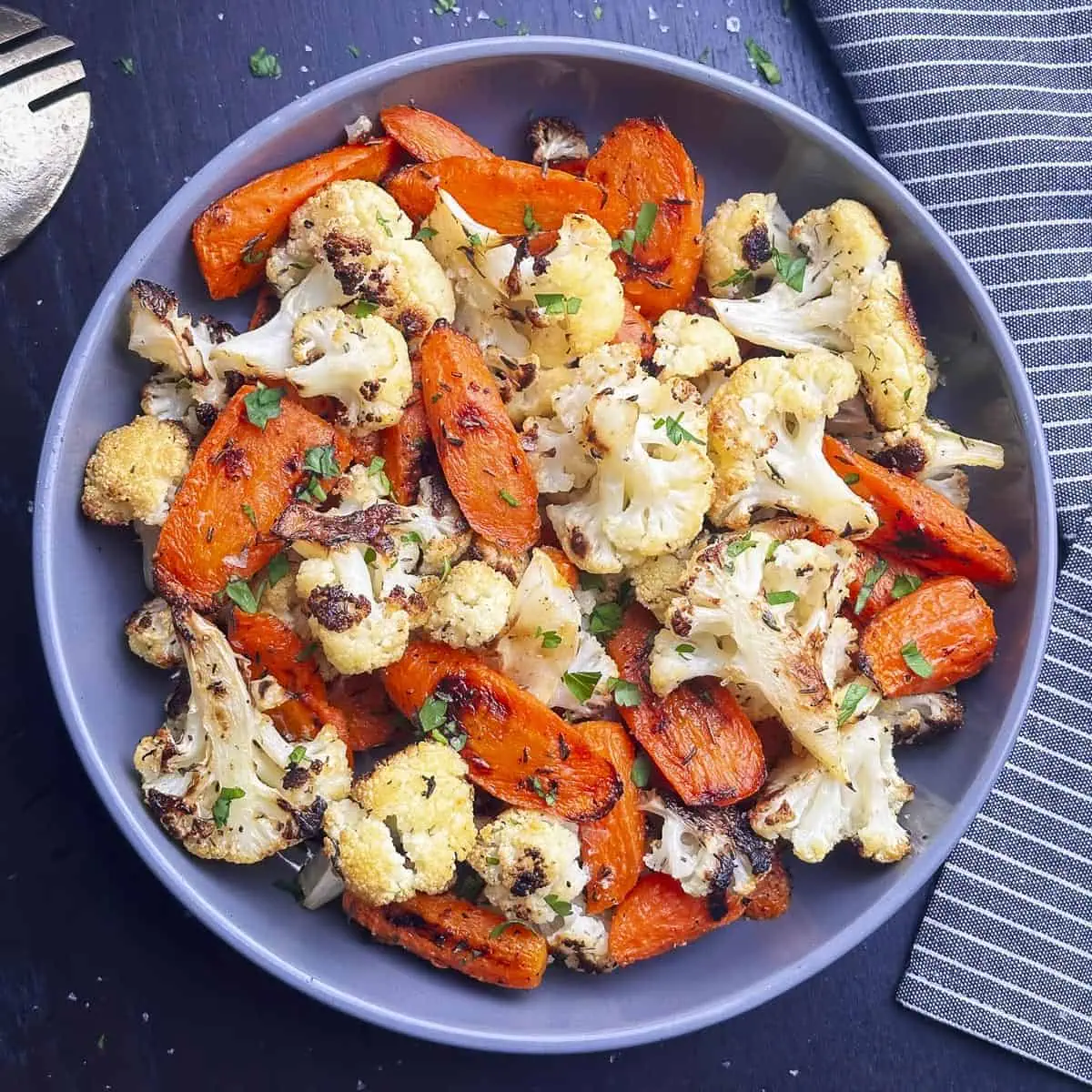 Roasted carrots and cauliflower in a grey bowl with parsley