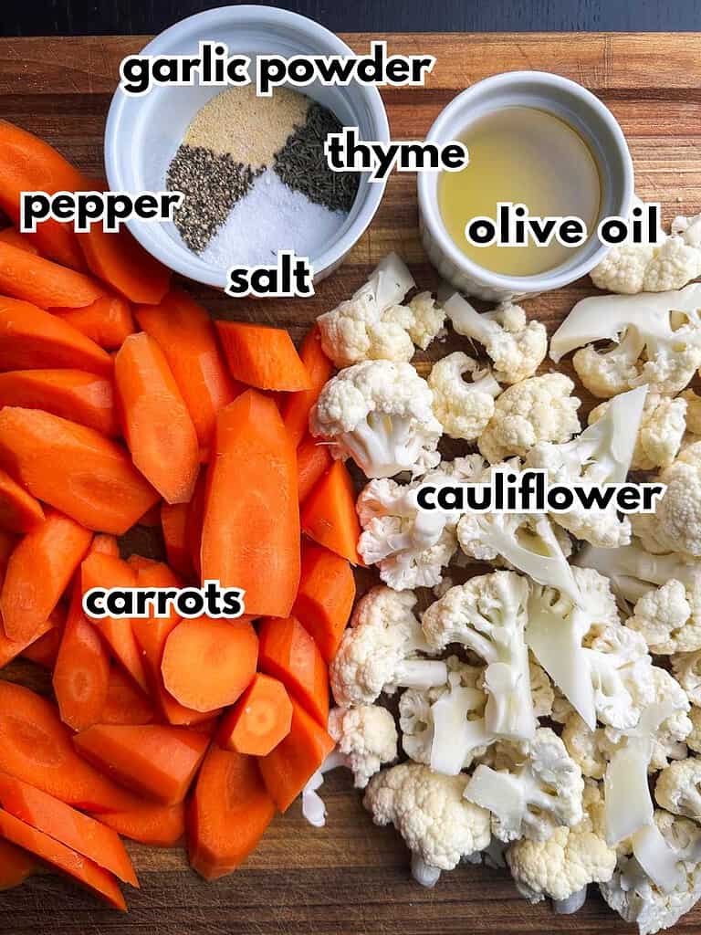 Sliced carrots, cauliflower florets, olive oil, and seasonings on a cutting board.