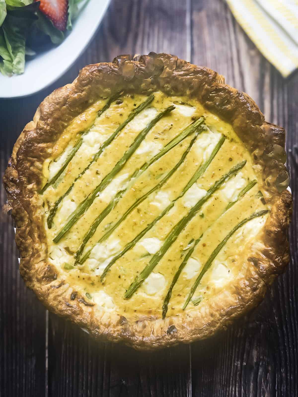 Overhead shot of asparagus ricotta tart on a wood table top.