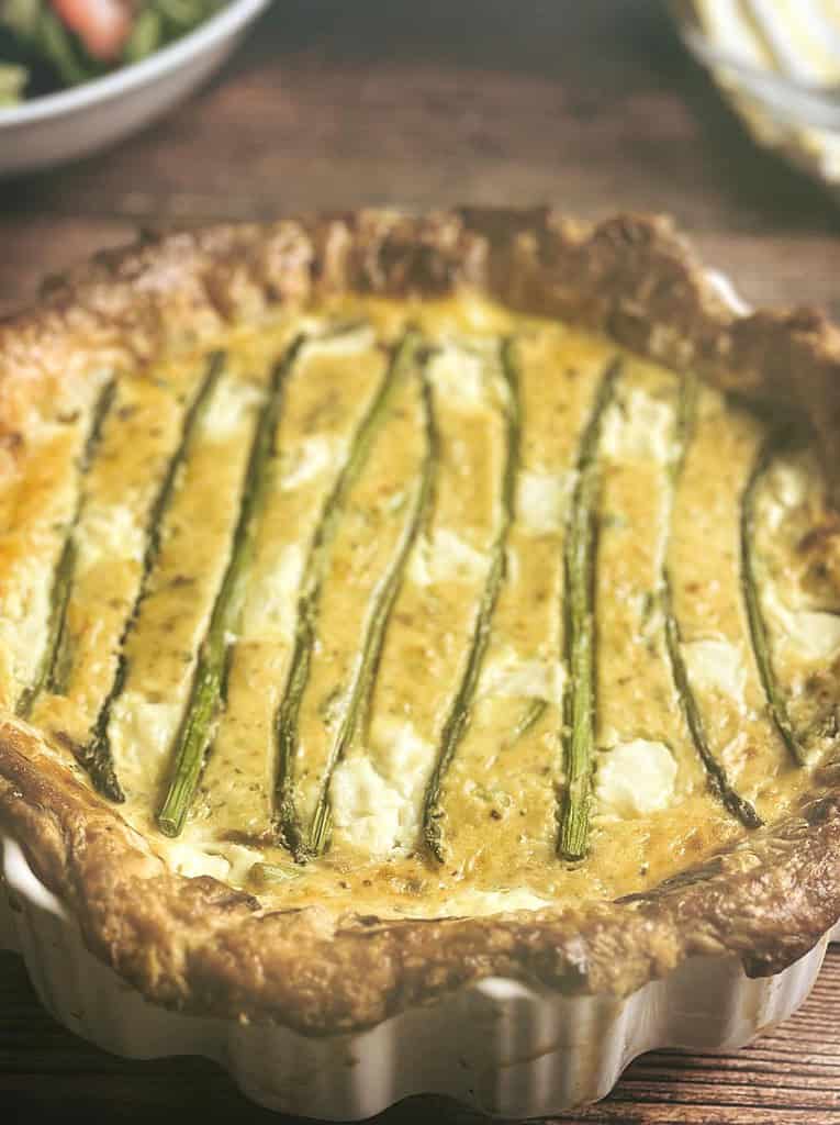 Side view of asparagus ricotta tart in a white tart dish.