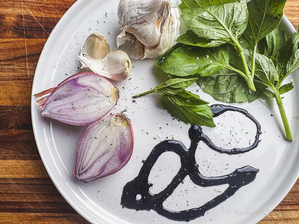 Fresh basil, shallots, garlic cloves, and a drizzle of balsamic glaze on a white plate.