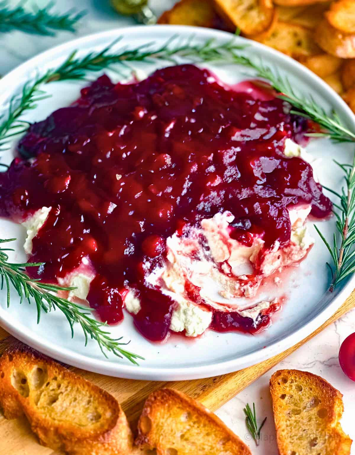 Cranberry whipped feta dip on a white plate with sprigs of rosemary.