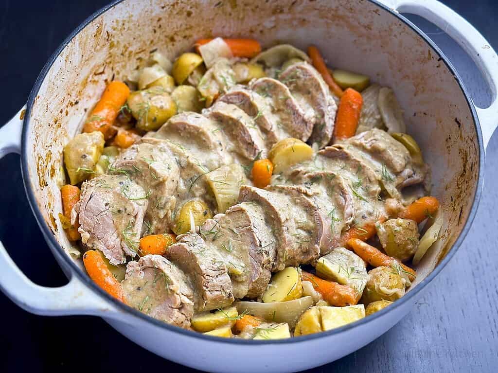Slices of pork tenderloin with vegetables and gravy in a Dutch oven.