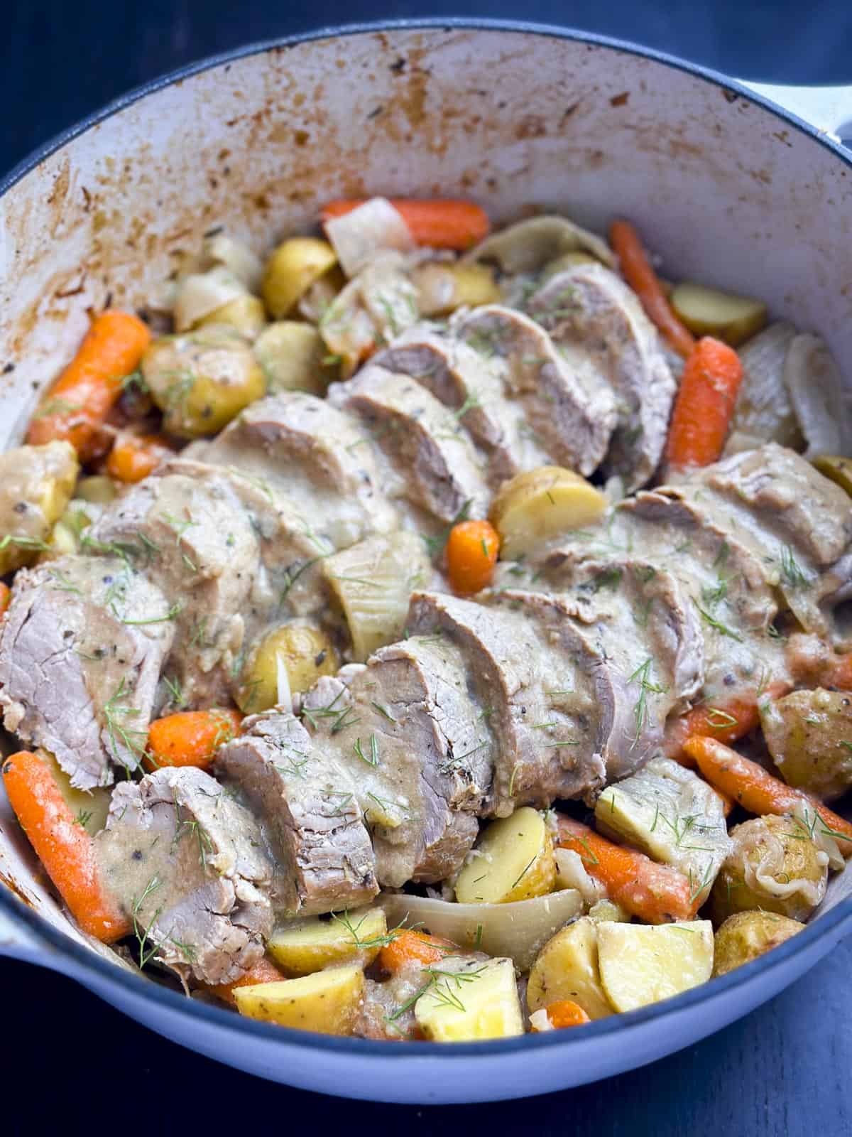 Pork tenderloin with gravy and roasted vegetables in a Dutch oven.