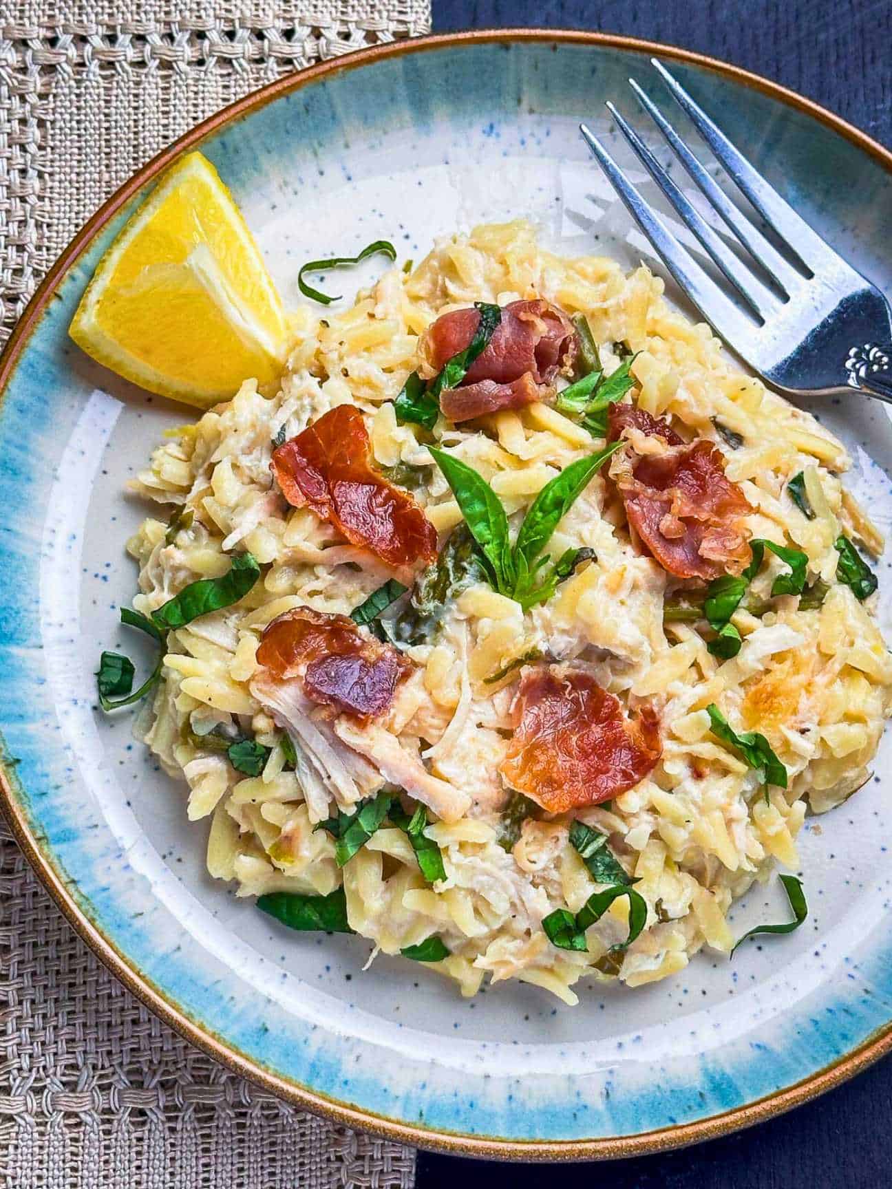 Creamy chicken orzo pasta on a plate with crispy prosciutto and basil on top.
