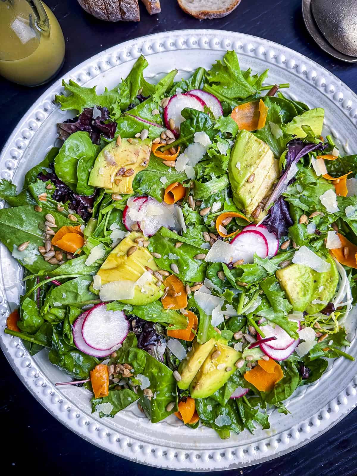 Mixed greens with carrots, radish, and avocado in a white bowl.