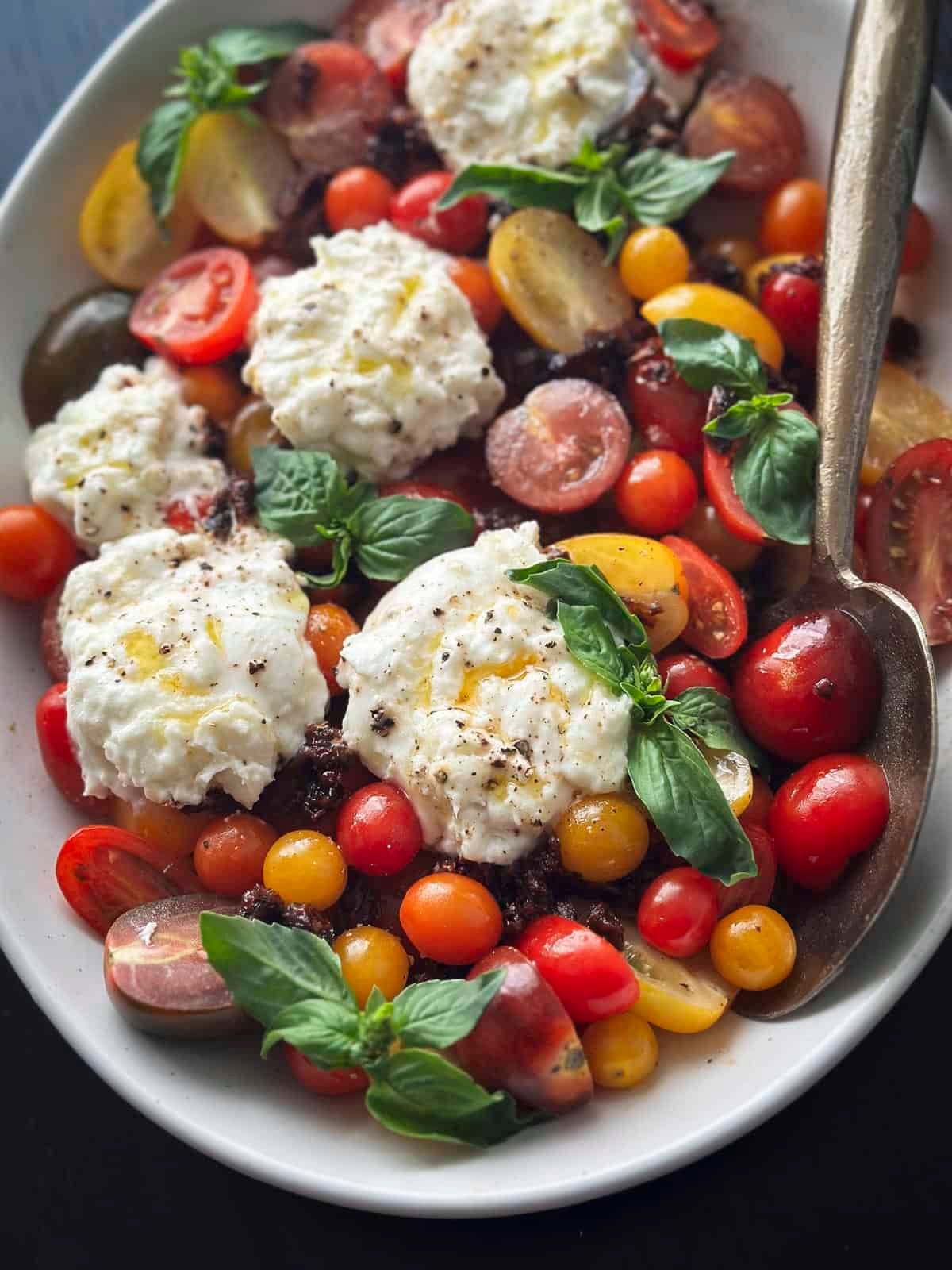 A plate of tomatoes, burrata cheese and basil.