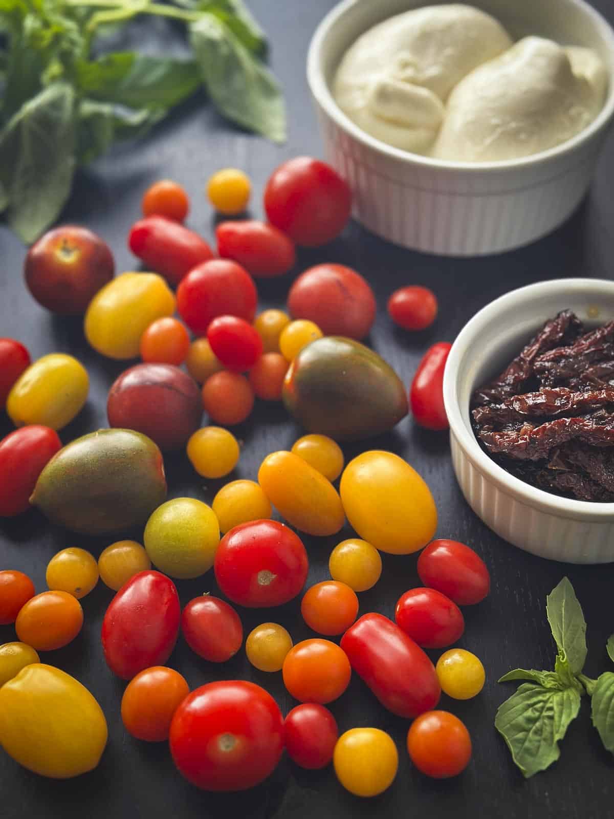Multicolored cherry tomatoes, sundried tomatoes, burrata, and basil.